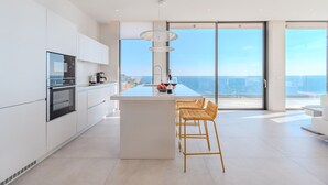 Una cocina moderna con una isla grande, armarios blancos y vistas al océano.