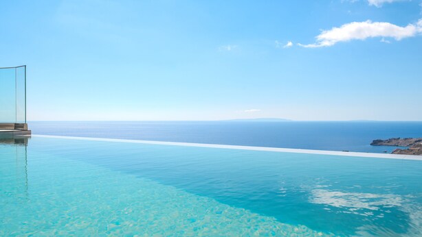 Una piscina infinita de color azul intenso con vista al mar y a una costa rocosa.