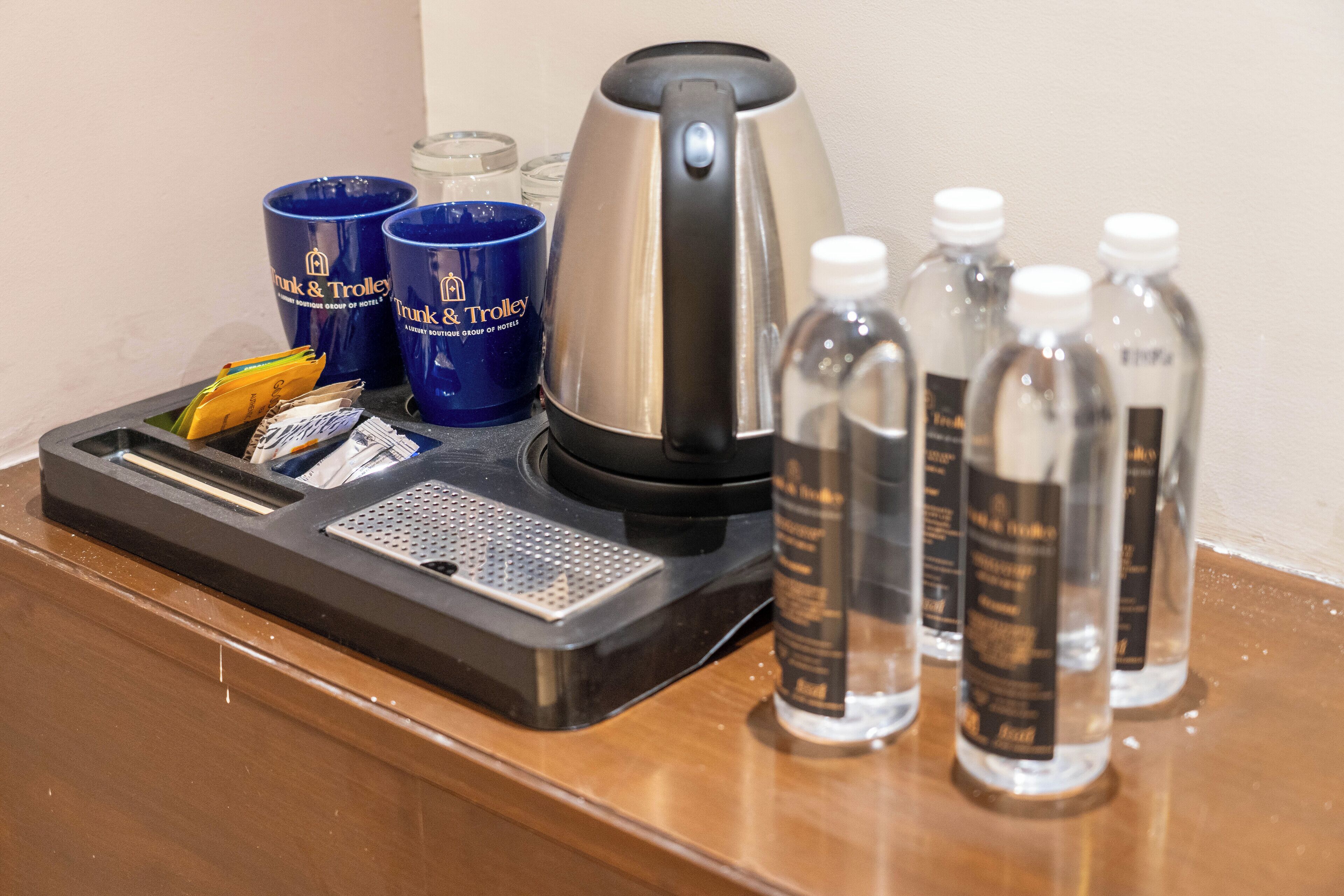 A hotel room's service tray with a kettle, two blue mugs, and three water bottles.