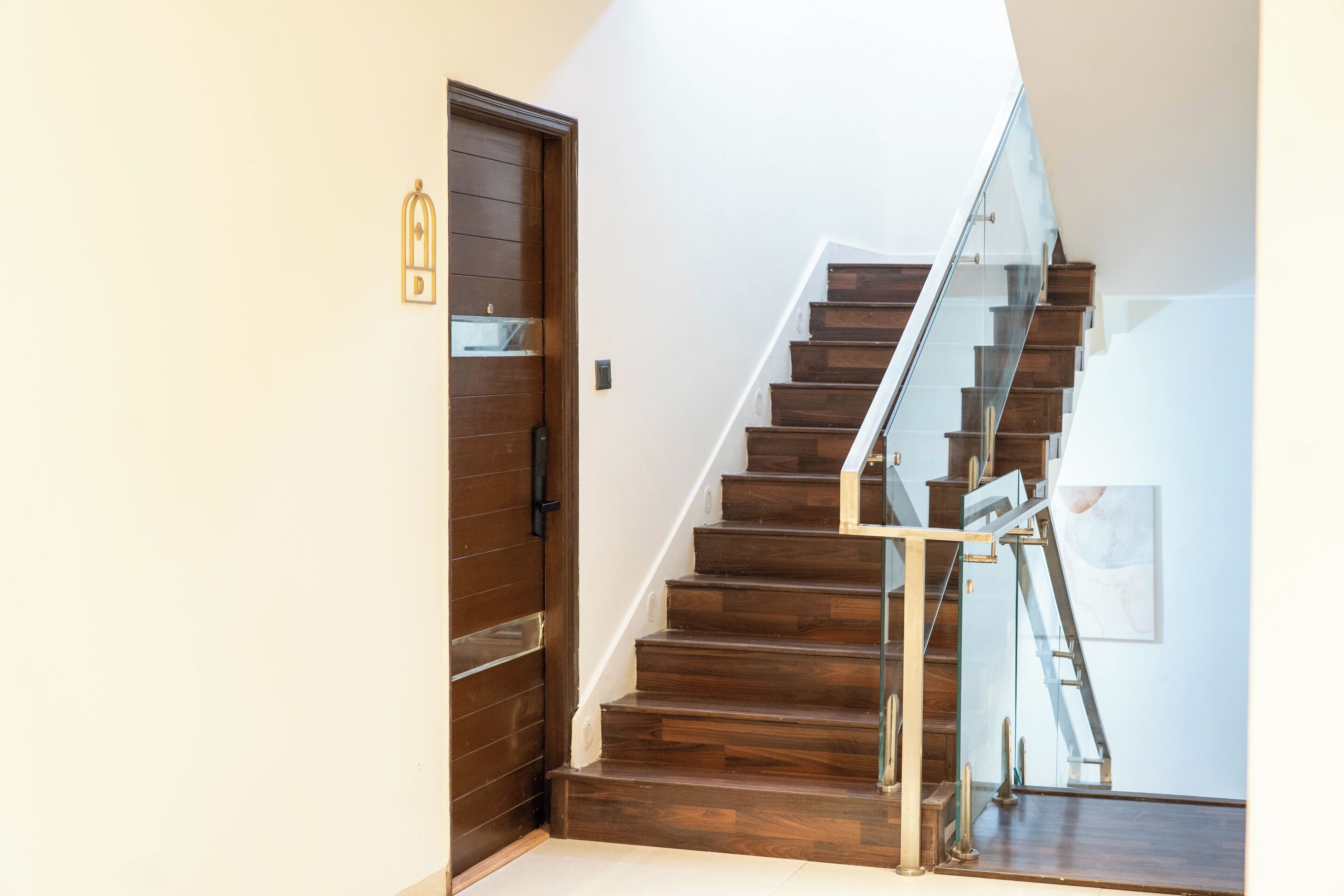 A modern staircase with wooden steps and glass railings, leading to a door with a brass handle.