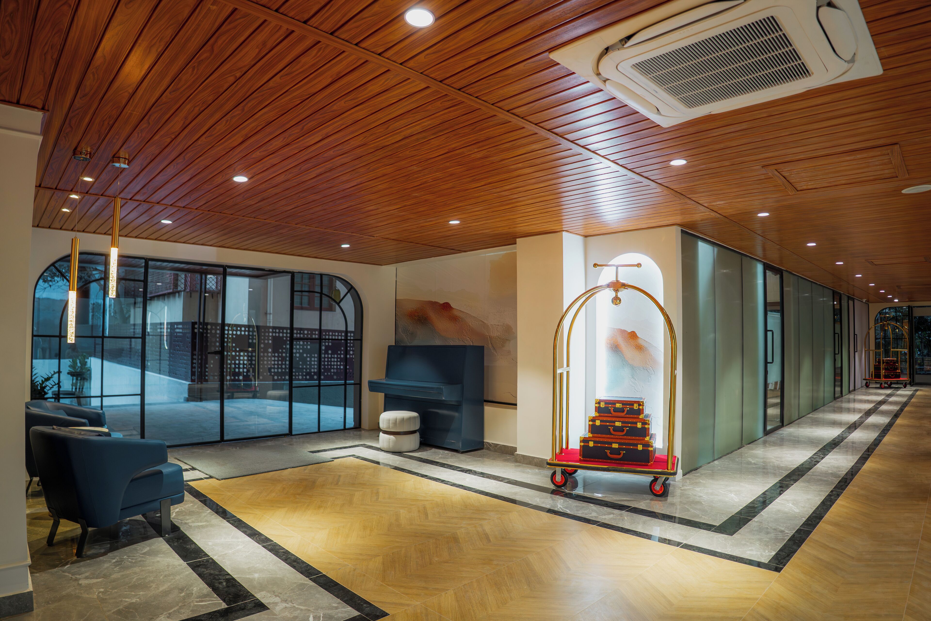 A spacious lobby with a wooden ceiling, a reception desk, a seating area, and a luggage cart.