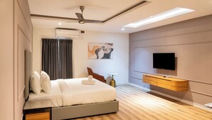 Una habitación de hotel moderna con una cama, un televisor de pantalla plana, un ventilador de techo y un equipo de aire acondicionado.