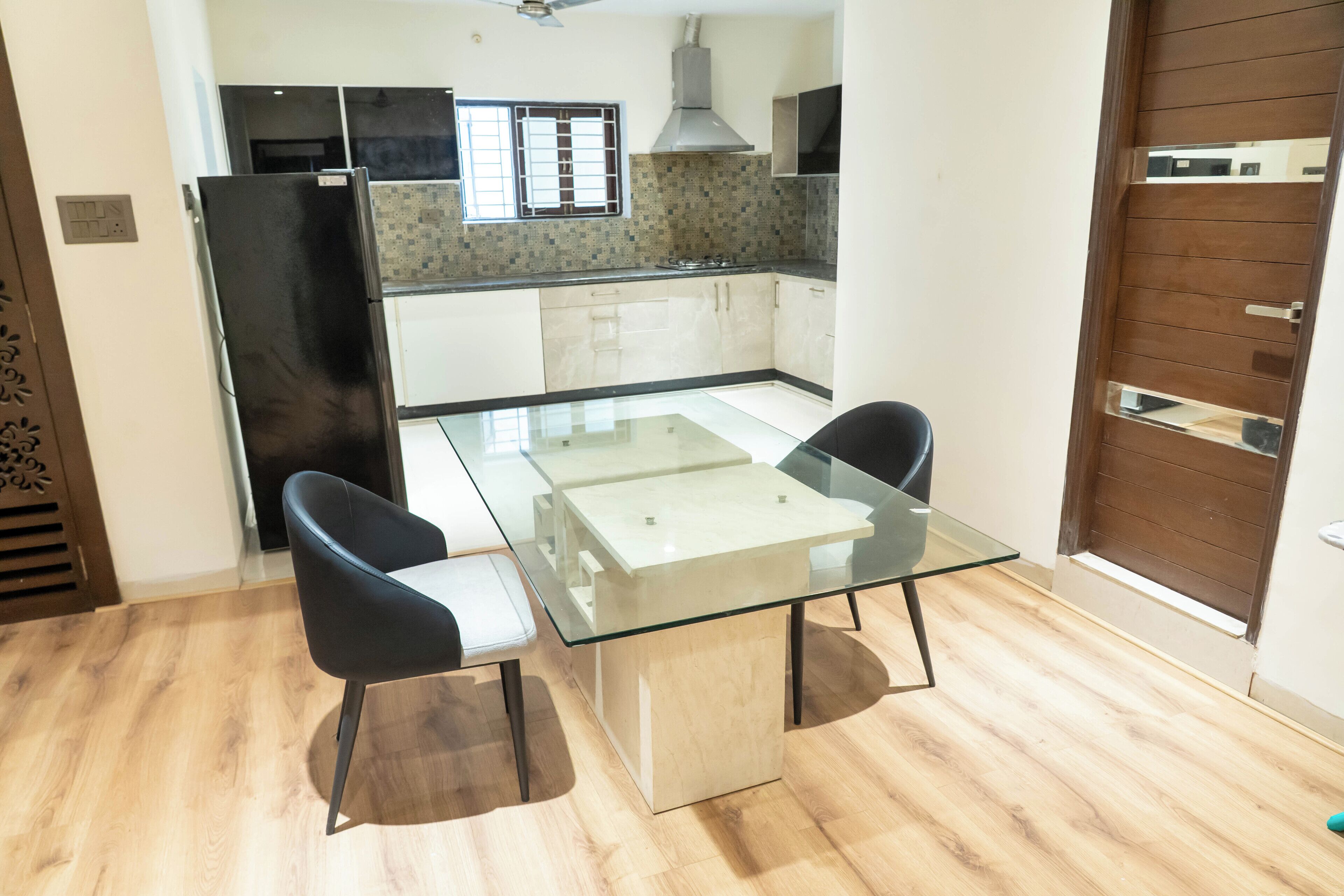 A modern kitchen with a glass dining table, two black chairs, and a black refrigerator.