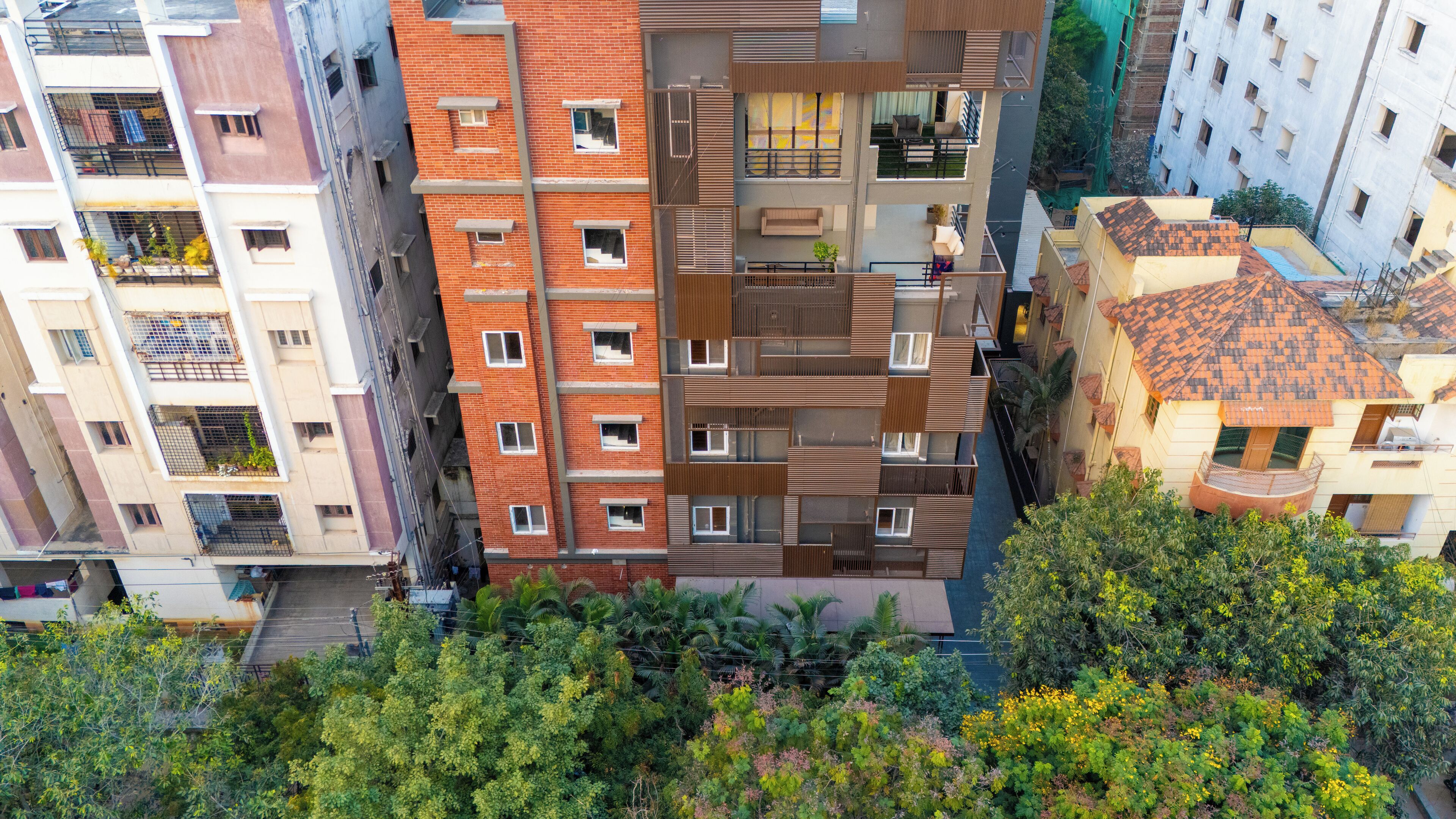 A multi-story residential building with balconies, a mix of brick and modern facade, and surrounding greenery.