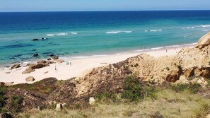A beach with clear turquoise waters, rocky cliffs, and sparse vegetation. - Vale Atlântico - BY SCH (Nazaré)