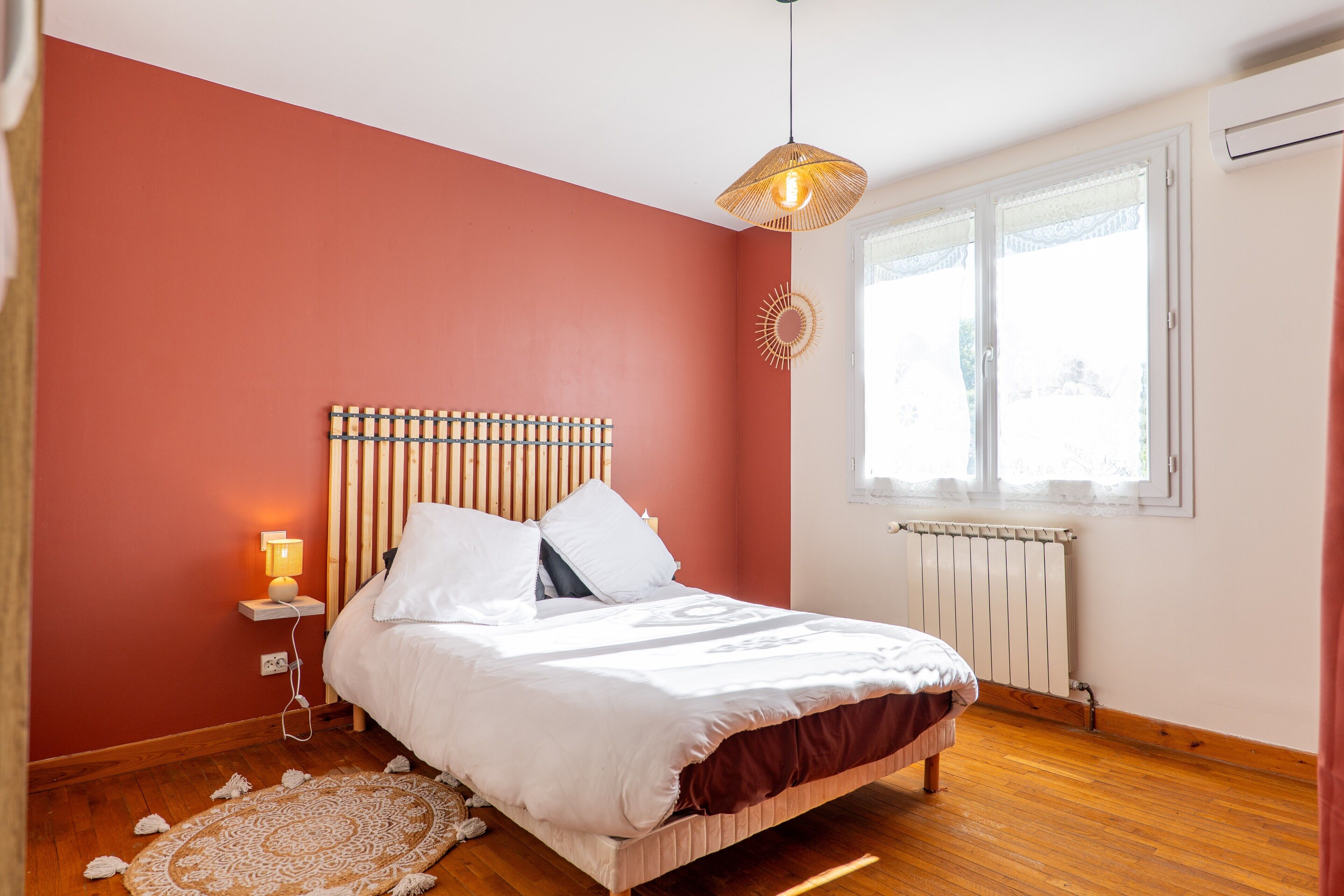 Een slaapkamer met een bed, een bedlamp, een radiator en een raam met gordijnen.