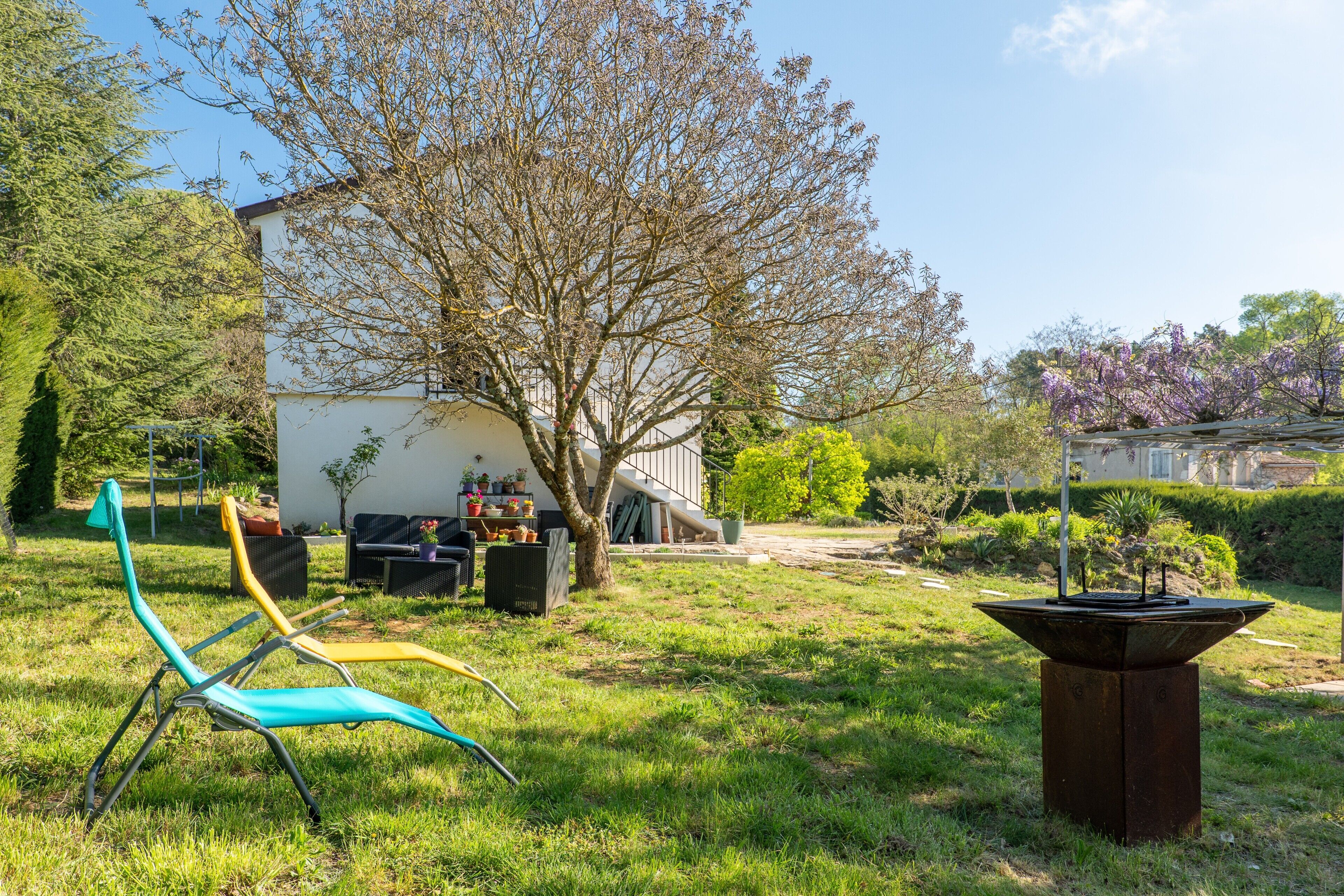 Un jardin avec du mobilier d’extérieur, un arbre et un bâtiment en arrière-plan.