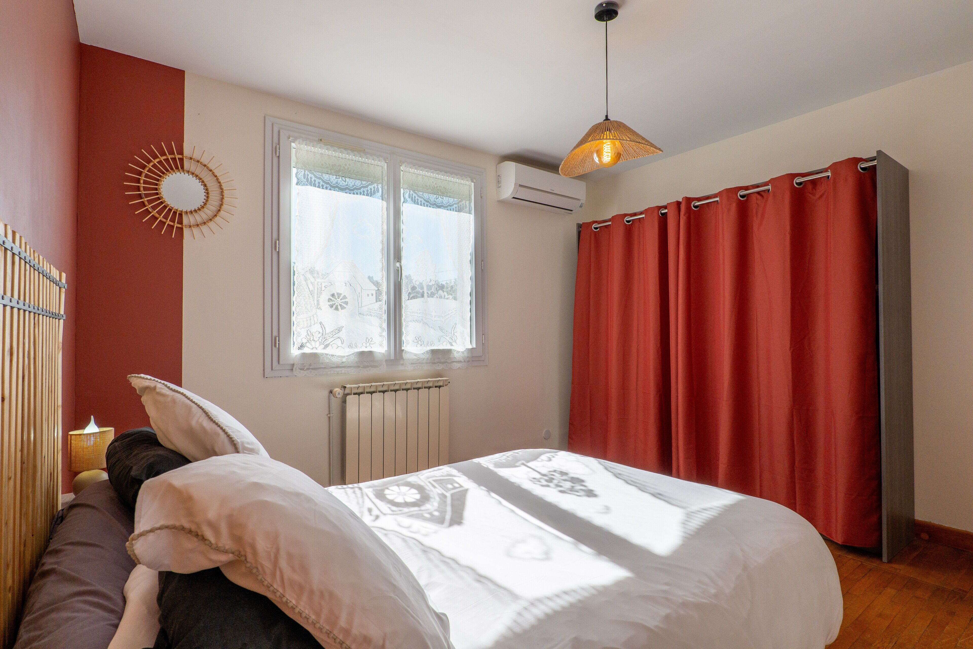 Une chambre à coucher avec un lit, une fenêtre, un climatiseur et un rideau rouge.