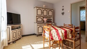 Een kamer met een televisie op een kast, een eettafel met stoelen en een dressoir.