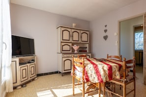 Ein Zimmer mit Fernseher auf einem Schrank, einem Esstisch mit Stühlen und einer Kommode.