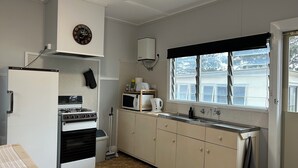 Una cocina compacta con estufa, horno, microondas y lavaplatos. Hay un reloj en la pared y una ventana con vistas al exterior.