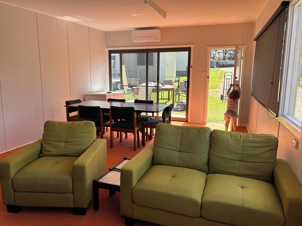 A room with a green sofa, a dining table with chairs, and a sliding glass door leading to an outdoor area.