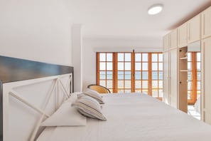 Ein Schlafzimmer mit Bett, Sessel und Meerblick durch große Fenster.