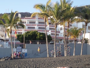 Ein Hotel direkt am Strand mit mehreren Stockwerken, Palmen und einem Sandstrand.