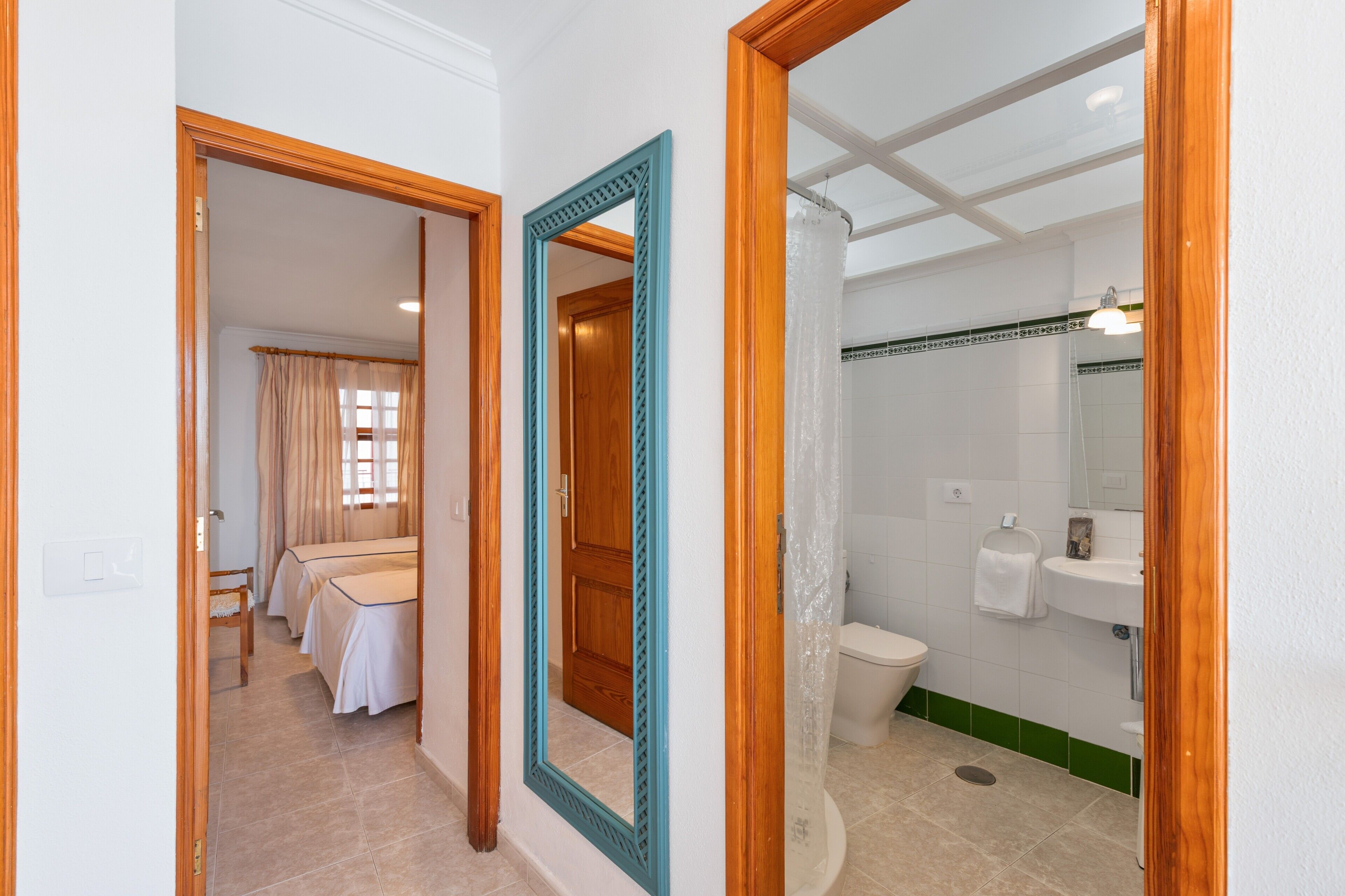 A hotel room with a wooden door, a mirror, a shower, a sink, and a toilet.