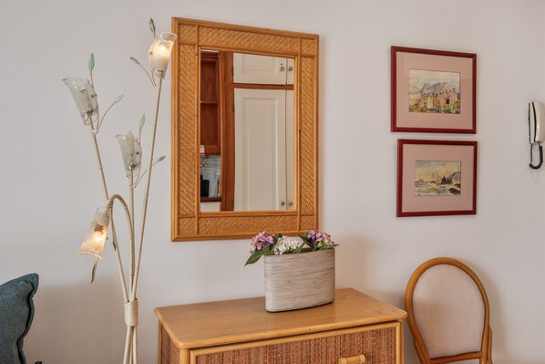A room with a wooden cabinet, a mirror, a wicker basket with flowers, and two framed pictures on the wall.