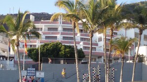 Un hotel frente al mar con varios pisos, palmeras y una playa de arena.