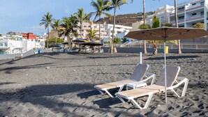 Una playa con tumbonas, sombrillas y palmeras.
