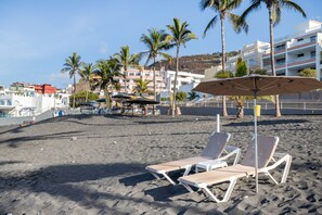 Ein Strand mit Liegestühlen, Sonnenschirmen und Palmen.