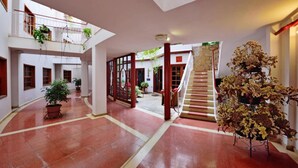 Un atrio amplio con una escalera, plantas en macetas y vistas al exterior.