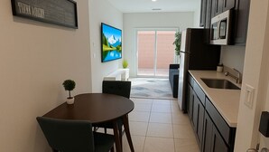 A modern kitchen with dark cabinets, a stainless steel sink, and a dining area with a round table and chairs. - BRAND NEW Comfy Guest House in a Great Location (Henderson)