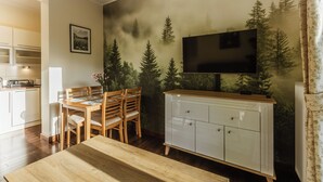 Un coin repas avec une table et des chaises en bois, un meuble blanc et un téléviseur fixé au mur.