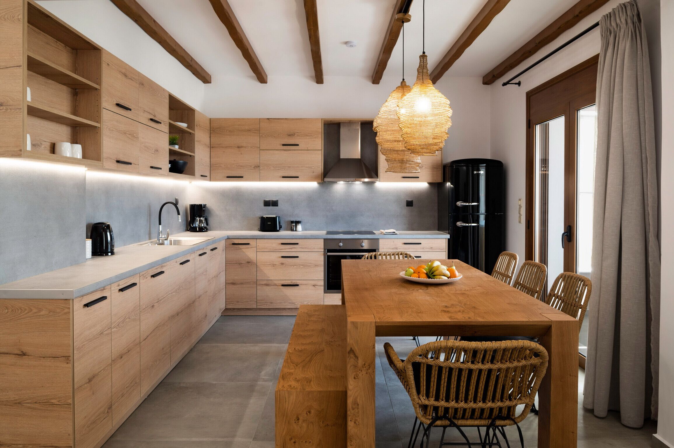Una cocina moderna con armarios de madera, una isla central y un comedor con sillas de mimbre.