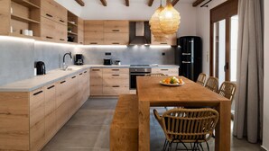 A modern kitchen with wooden cabinets, a central island, and a dining area with wicker chairs. - Zen Luxury Home (Rethymno)