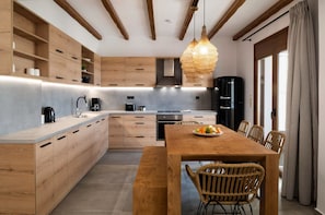 A modern kitchen with wooden cabinets, a central island, and a dining area with wicker chairs. - Zen Luxury Home (Rethymno)