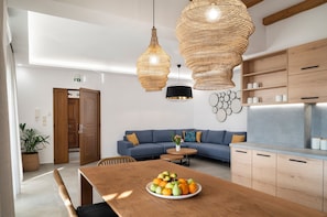 A modern kitchen with wooden cabinets, a dining table with a fruit bowl, and a blue sofa. - Zen Luxury Home (Rethymno)