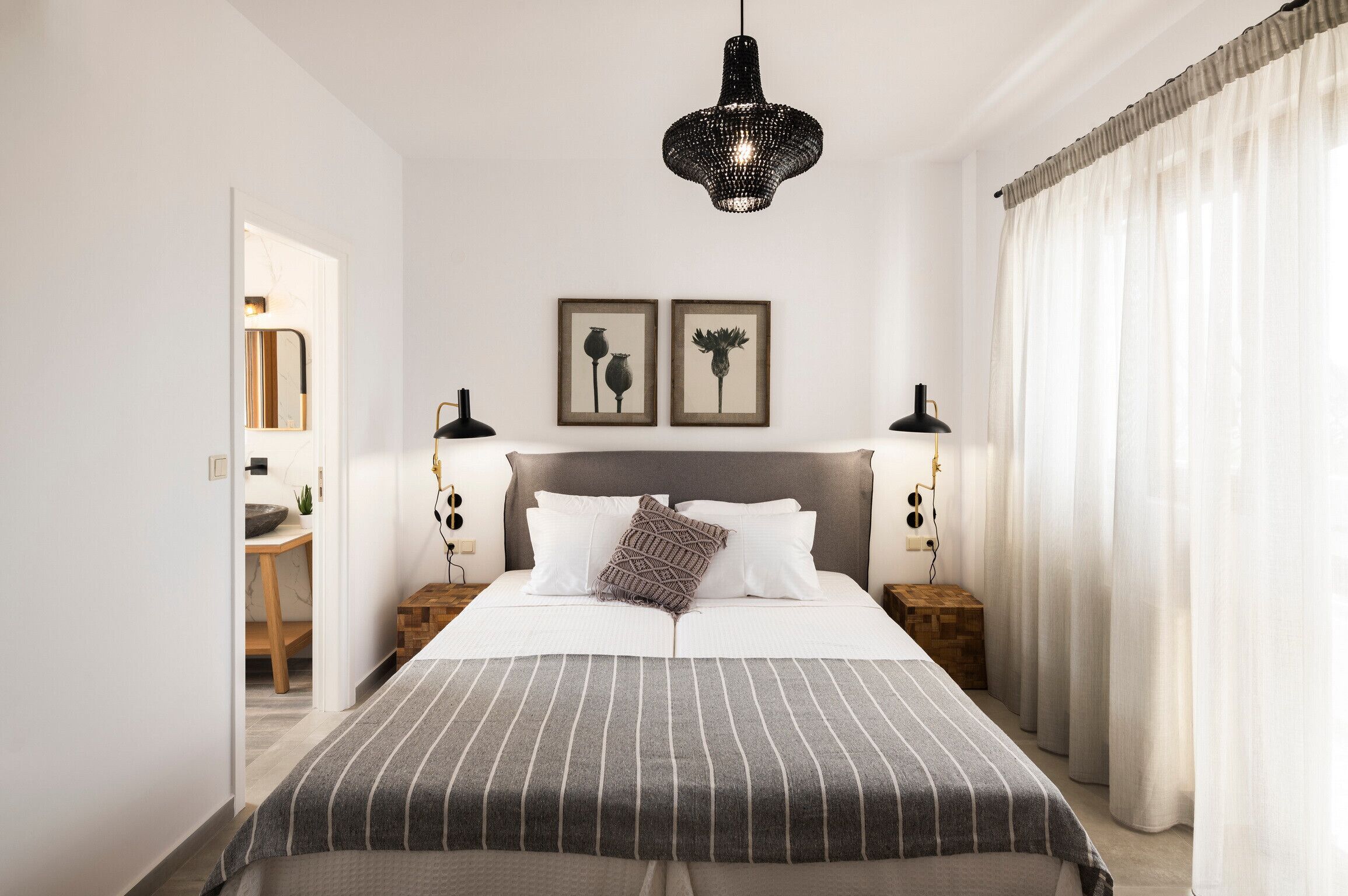 Un dormitorio ordenado con una cama grande, dos mesitas de noche, una lámpara colgante y dos cuadros en la pared.
