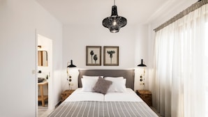 A neatly arranged bedroom with a large bed, two bedside tables, a hanging light fixture, and two framed pictures on the wall. - Zen Luxury Home (Rethymno)