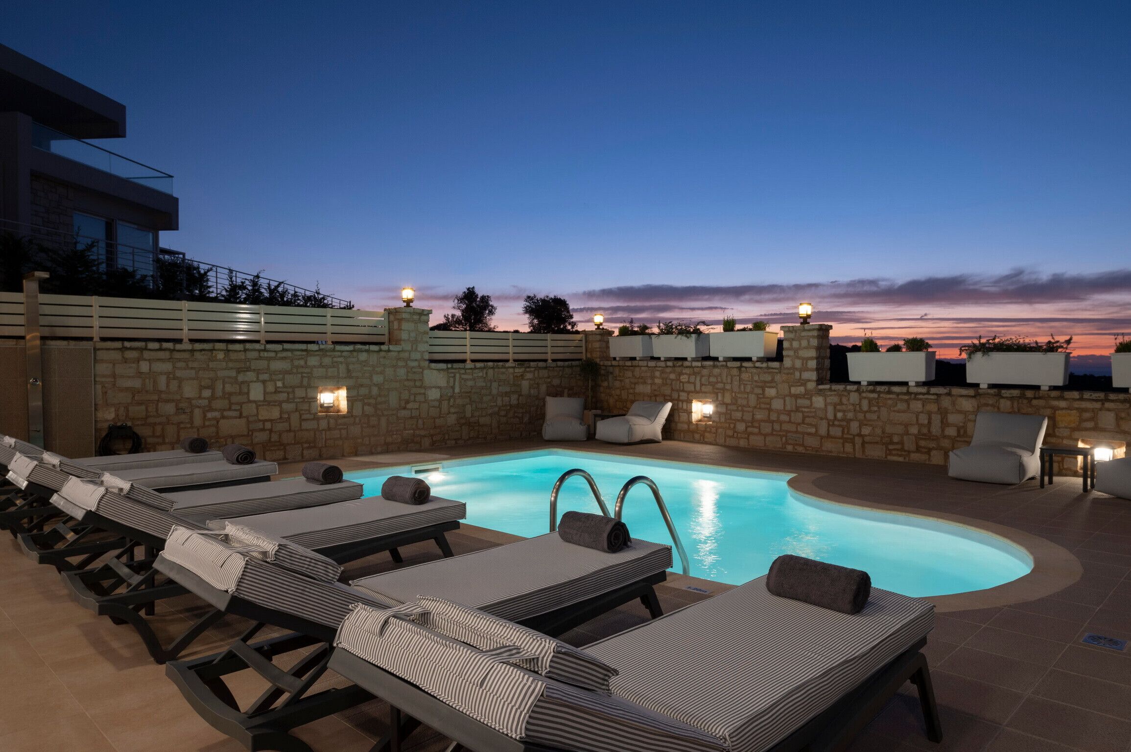 Un área junto a la piscina con sillones de descanso y un muro de piedra.