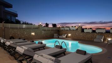 Un área junto a la piscina con sillones de descanso y un muro de piedra.