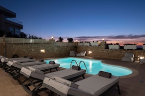 A poolside area with lounge chairs and a stone wall. - Zen Luxury Home (Rethymno)