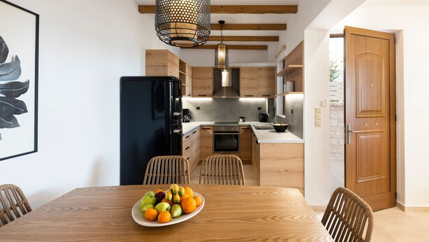 Una cocina moderna con armarios de madera, un refrigerador negro y una zona de comedor con una mesa y sillas de madera.