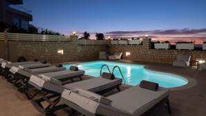 Un área junto a la piscina con sillas de descanso y un muro de piedra.