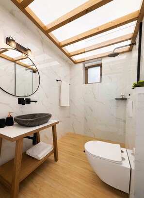 Ein modernes Badezimmer mit Dachfenster, einem runden Spiegel, einem Holzlager und einer weißen Toilette sowie einer Duschkabine.