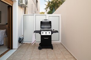 Ein tragbarer Grill in einem schmalen Außenbereich mit Fliesenboden, einer weißen Tür und einer weißen Wand.
