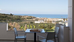 Un balcón con dos sillas y una mesa, con vistas a un paisaje costero con edificios y vegetación.