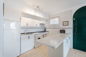 Una cocina con armarios blancos, lavadora, microondas y una puerta verde.