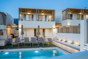 A modern outdoor pool area with lounge chairs and a dining set. - Corallia Villas (Agios Vasileios)