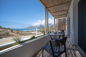 A balcony with a view of the sea and mountains, a table, and chairs. - Corallia Villas (Agios Vasileios)
