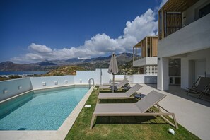 A modern outdoor pool area with lounge chairs and a view of mountains and a body of water. - Corallia Villas (Agios Vasileios)