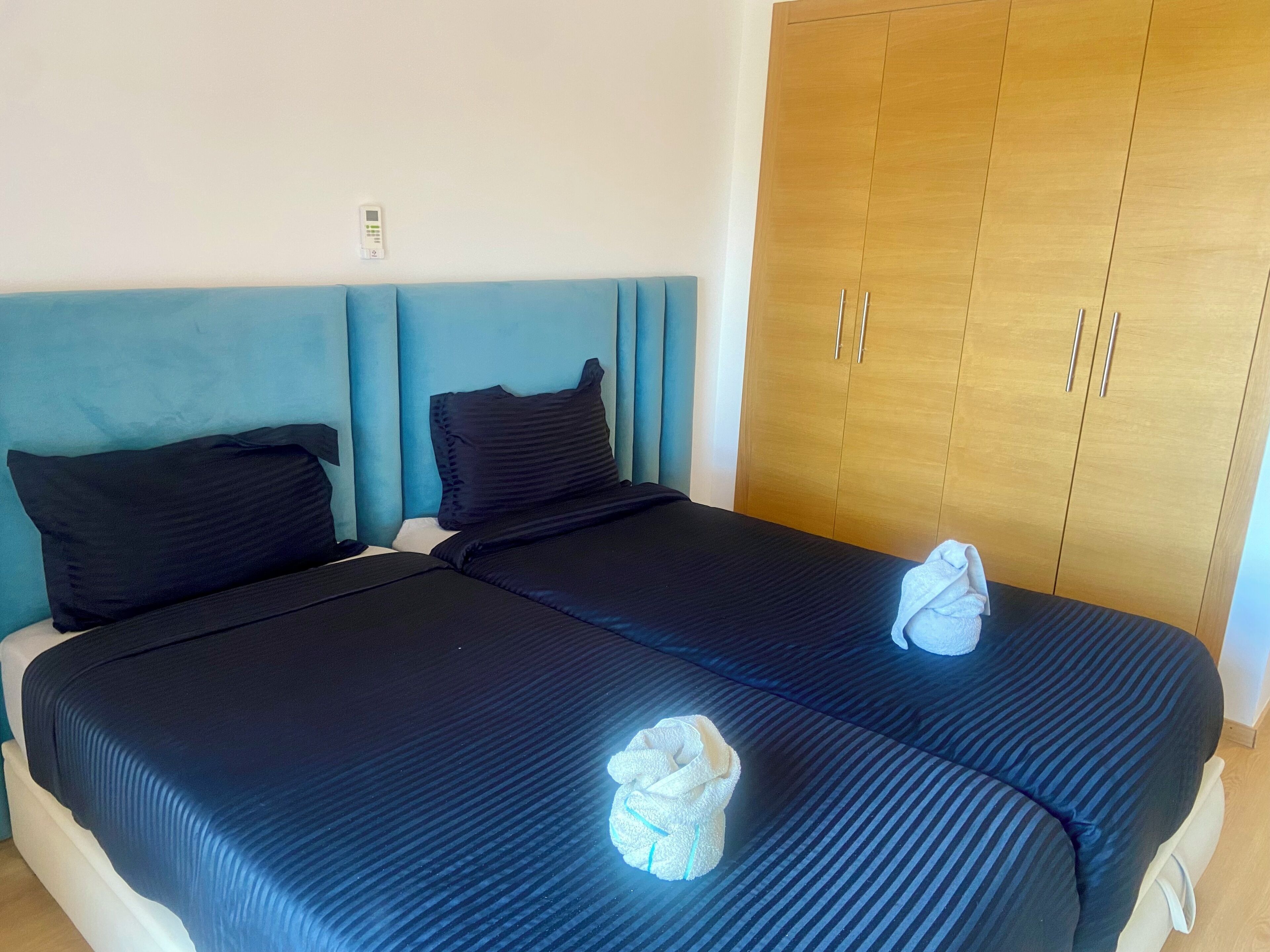 A hotel room with a bed, two pillows, a headboard, a wardrobe, and a towel on the bed.