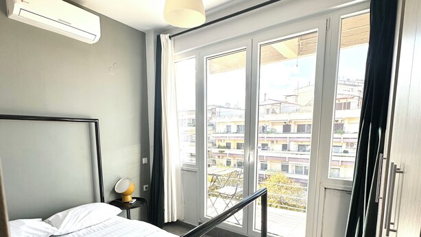 Une chambre moderne avec un lit, une table de chevet et une vue sur la ville grâce à de grandes fenêtres.