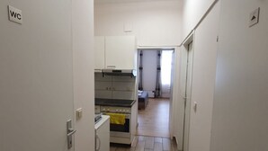 Um corredor estreito que leva a uma cozinha com armários brancos, fogão e forno pequeno.