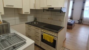Cozinha compacta com pia, fogão e forno, uma pequena área de refeições e vista para um quarto com cortinas.