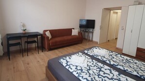 Quarto de hotel com cama, sofá, televisão, escrivaninha e guarda-roupa.