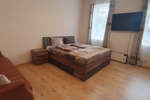 A bedroom with a wooden bed, a nightstand, a TV, and a window with curtains. - Quaint 1BR in Simmering -Well-suited for Longstays (Vienna)